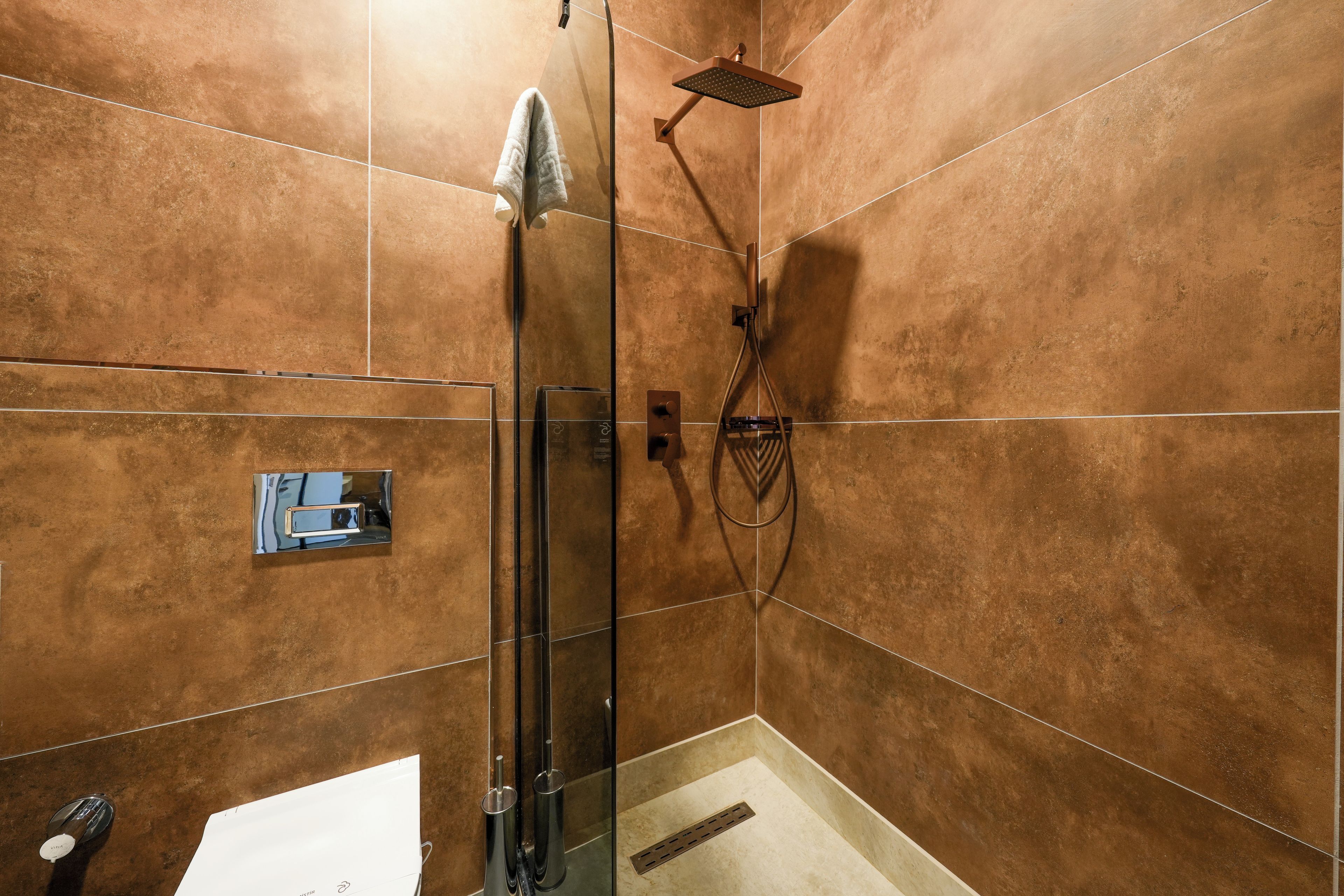 A shower with a glass door, a handheld showerhead, and a wall-mounted control panel.