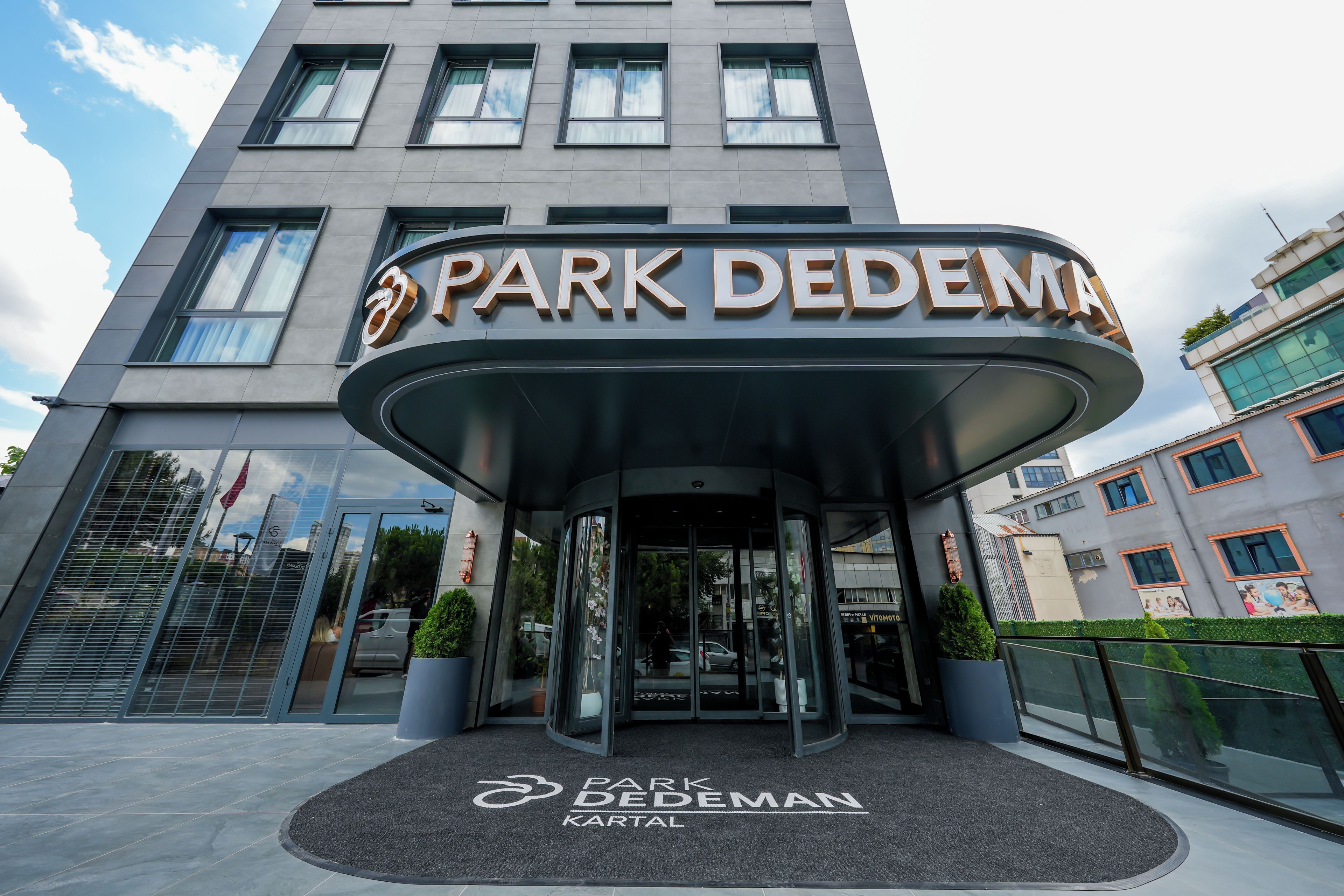 A modern hotel entrance with a curved canopy and a sign reading 'Park DedeMan Kartal'.