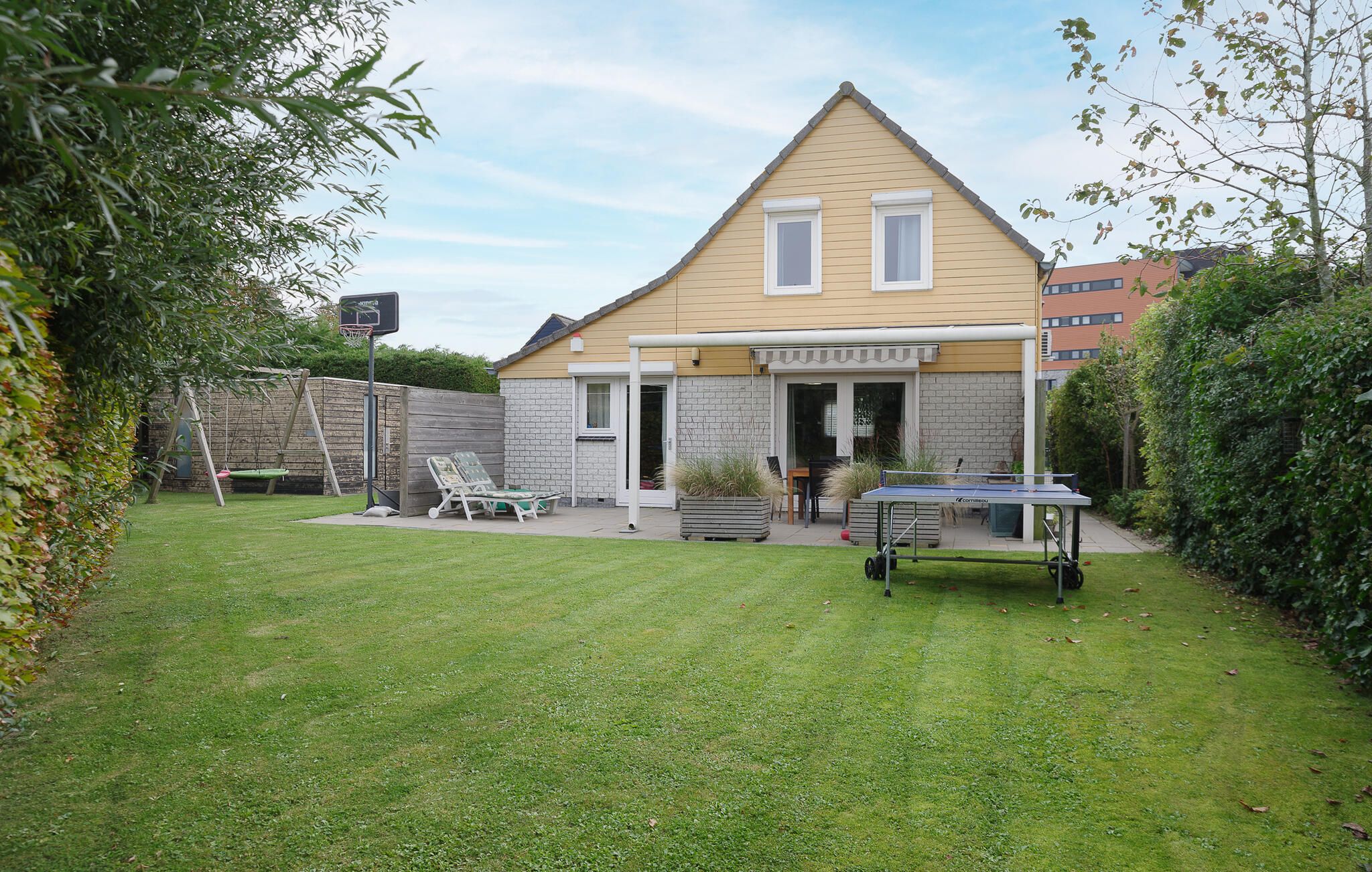 Ein Wohnhaus mit einem zweistöckigen Gebäude, einer Terrasse mit Gartenmöbeln und einem Basketballkorb.