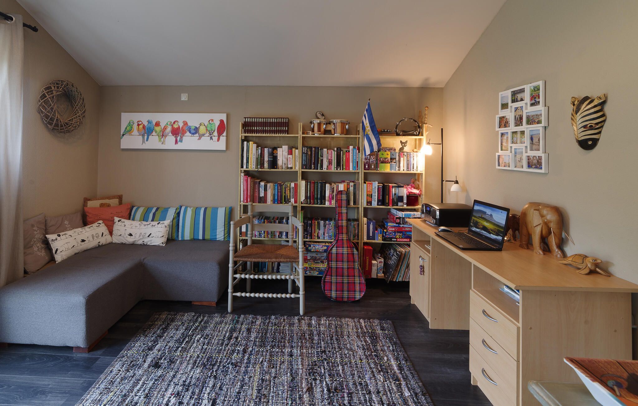 Ein gemütliches Zimmer mit einem Bett, einem Schreibtisch mit einem Laptop, einem Bücherregal und einer Wand mit Bildern.