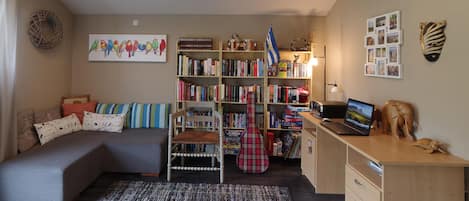 Ein gemütliches Zimmer mit einem Bett, einem Schreibtisch mit einem Laptop, einem Bücherregal und einer Wand mit Bildern.