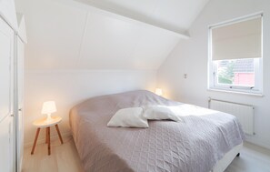 Ein Schlafzimmer mit einem Bett, einem Nachttisch mit Lampe, einem Fenster und einer Heizung.