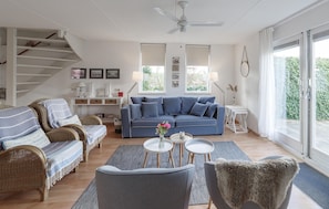 Uma sala de estar moderna com um sofá azul, mobiliário de vime, um ventilador de teto e janelas amplas.
