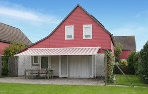 Ein rotes Haus mit einer überdachten Terrasse, einer Ziegelwand und einem Holzzaun.