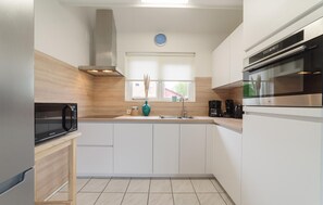 A modern kitchen with white cabinets, a stainless steel range hood, a microwave, a sink, and a window with a view of the outside. - 3 bedroom stunning home in Wemeldinge (Wemeldinge)