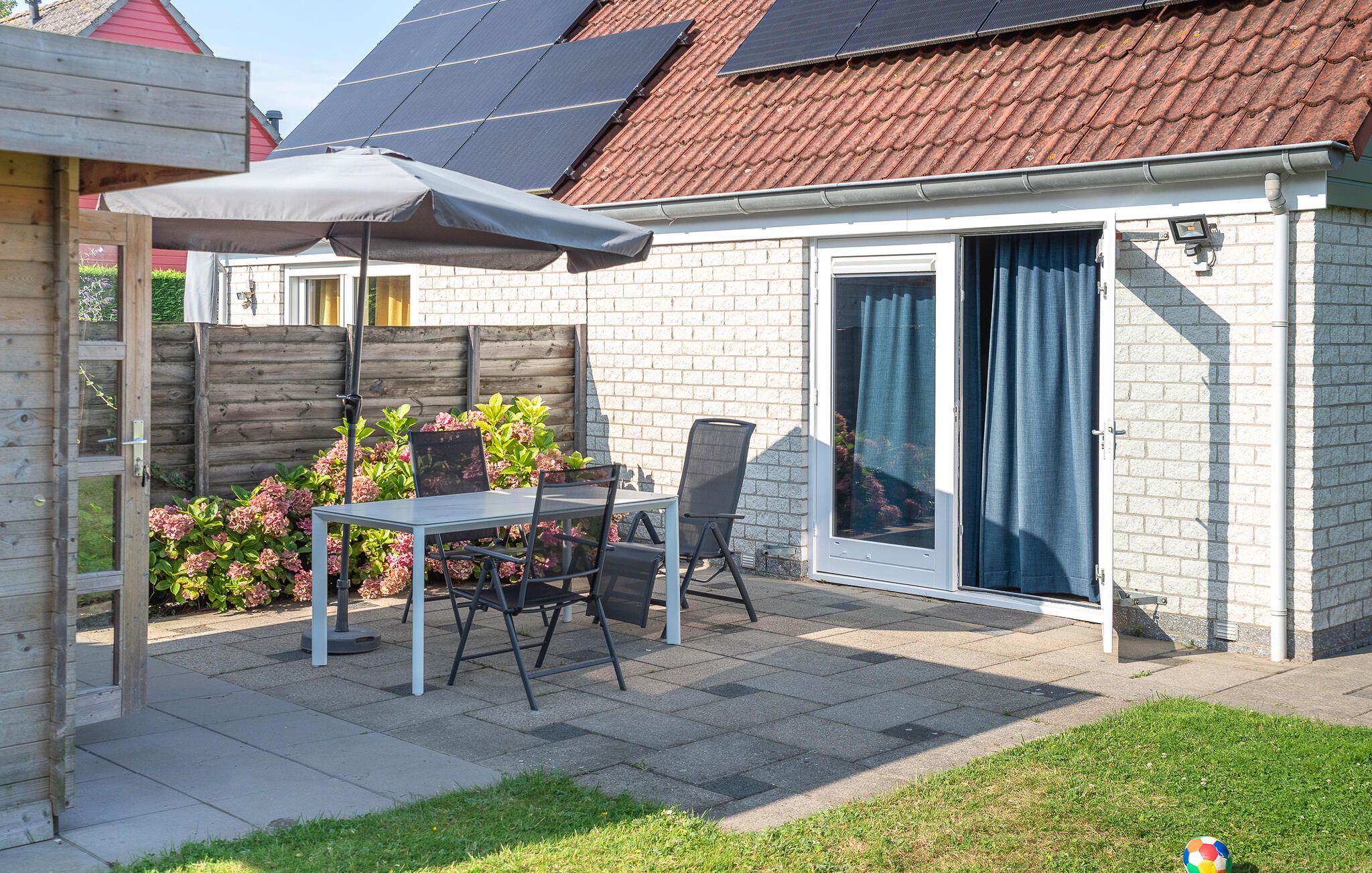 A patio with a table and chairs, a covered umbrella, a brick wall, and a sliding glass door.
