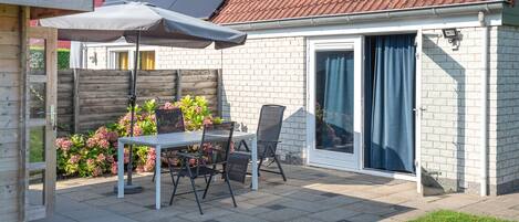 A patio with a table and chairs, a covered umbrella, a brick wall, and a sliding glass door.