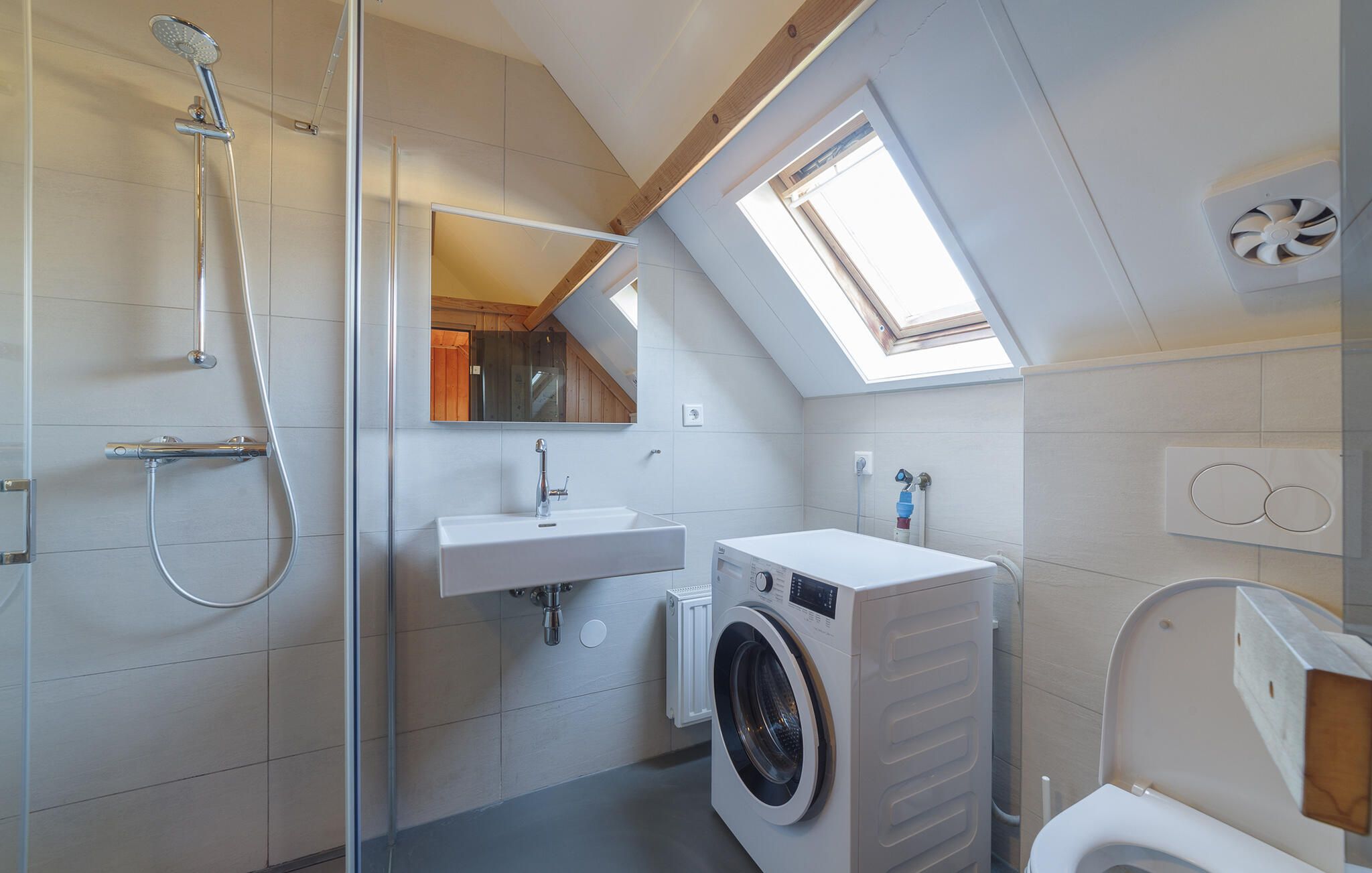A compact bathroom with a shower, a sink, a washing machine, and a toilet.