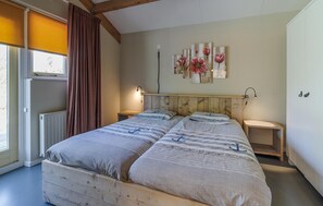 Un llit doble amb capçalera de fusta, dues taules de nit, un radiador, una finestra amb cortines i una paret amb obra d'art floral.