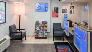 Un'area reception con scrivania, sedie, porta riviste e uno schermo digitale che mostra informazioni.