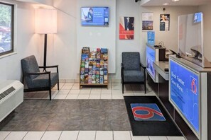 Zona de recepción con un mostrador, sillas, un atril para revistas y una pantalla digital que muestra información.