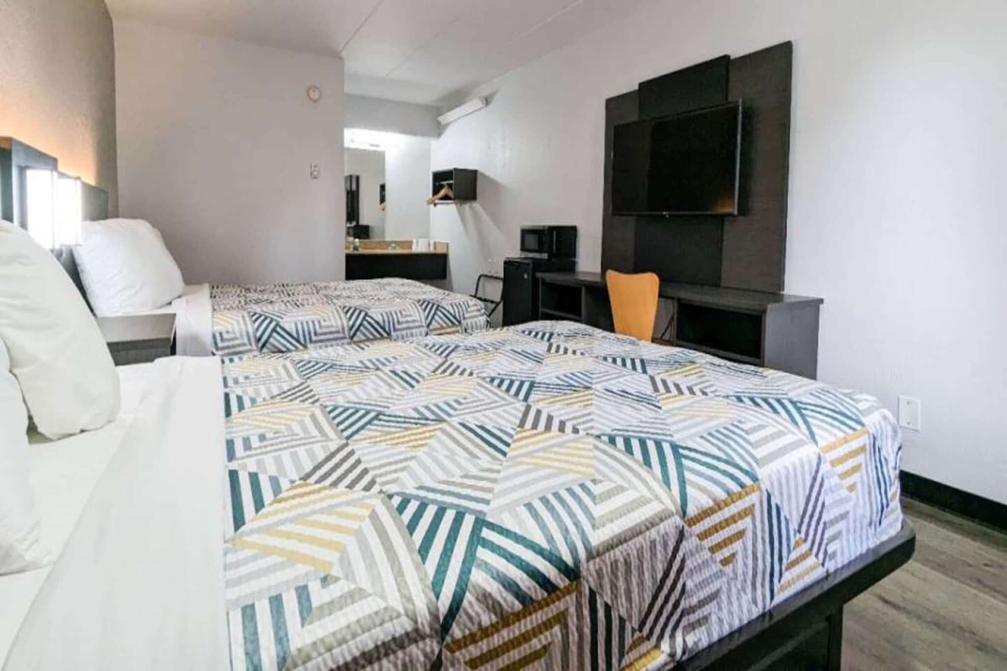 Habitación de hotel con dos camas, un escritorio, una silla, un televisor y un espejo.