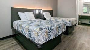 Una camera d'albergo con due letti, un comodino, una lampada a parete e una finestra con vista.