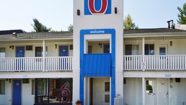 Un motel con un grande cartello con il numero '6', un cartello di 'benvenuto' e un cartello con la scritta 'divieto di sosta notturna'.