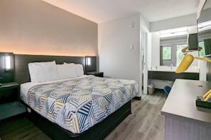 Habitación de hotel con cama, mesita de noche, lámpara y vistas al exterior.