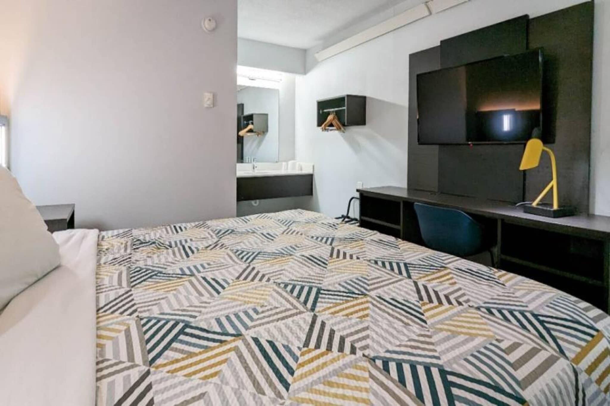 A hotel room with a bed, a desk, a chair, a TV, and a mirror.