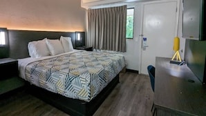 Una camera d'albergo con un letto, una scrivania, una sedia, una televisione e una finestra con tende.