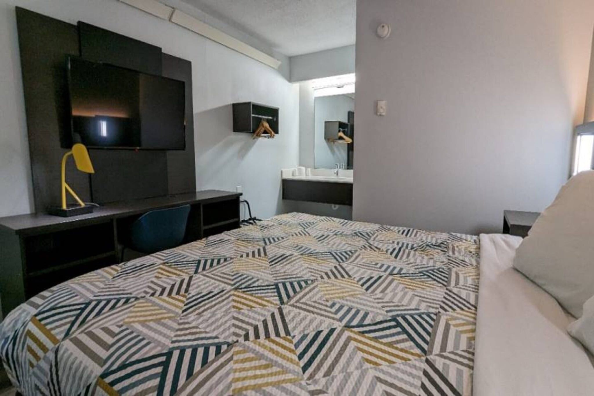 Een hotelkamer met een bed, een bureau, een stoel, een televisie, een spiegel en een badkamer.