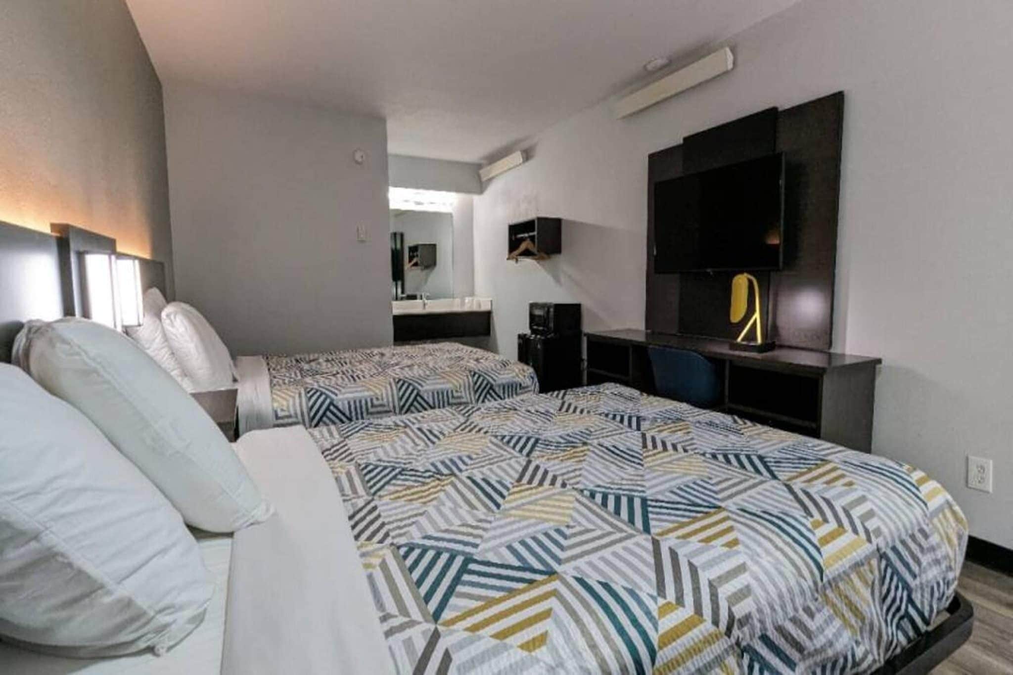 A hotel room with two beds, a TV, a desk, and a mirror.
