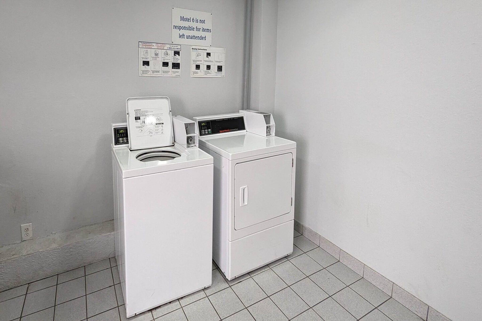 A laundry area with a front-loading washer and dryer, a sign indicating the motel's policy on unattended items, and a wall-mounted information board.