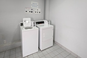A laundry area with a front-loading washer and dryer, a sign indicating the motel's policy on unattended items, and a wall-mounted information board.