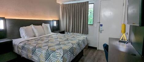 Une chambre d’hôtel avec un lit, un bureau, une chaise, une fenêtre avec des rideaux et une porte.
