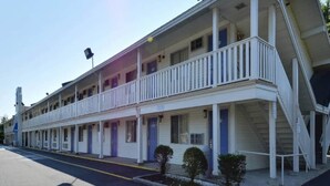 Un motel con estructura de dos pisos, varias habitaciones con puertas individuales y un porche cubierto.