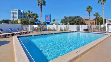 A swimming pool with lounge chairs, a fence, and a building in the background.