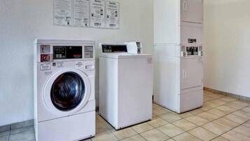 A laundry facility with a front-loading washing machine and a dryer, a cabinet with a control panel, and informational posters on the wall.