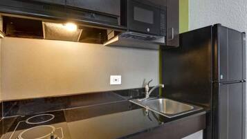 A modern kitchen with a black refrigerator, stainless steel sink, and a microwave above the counter.