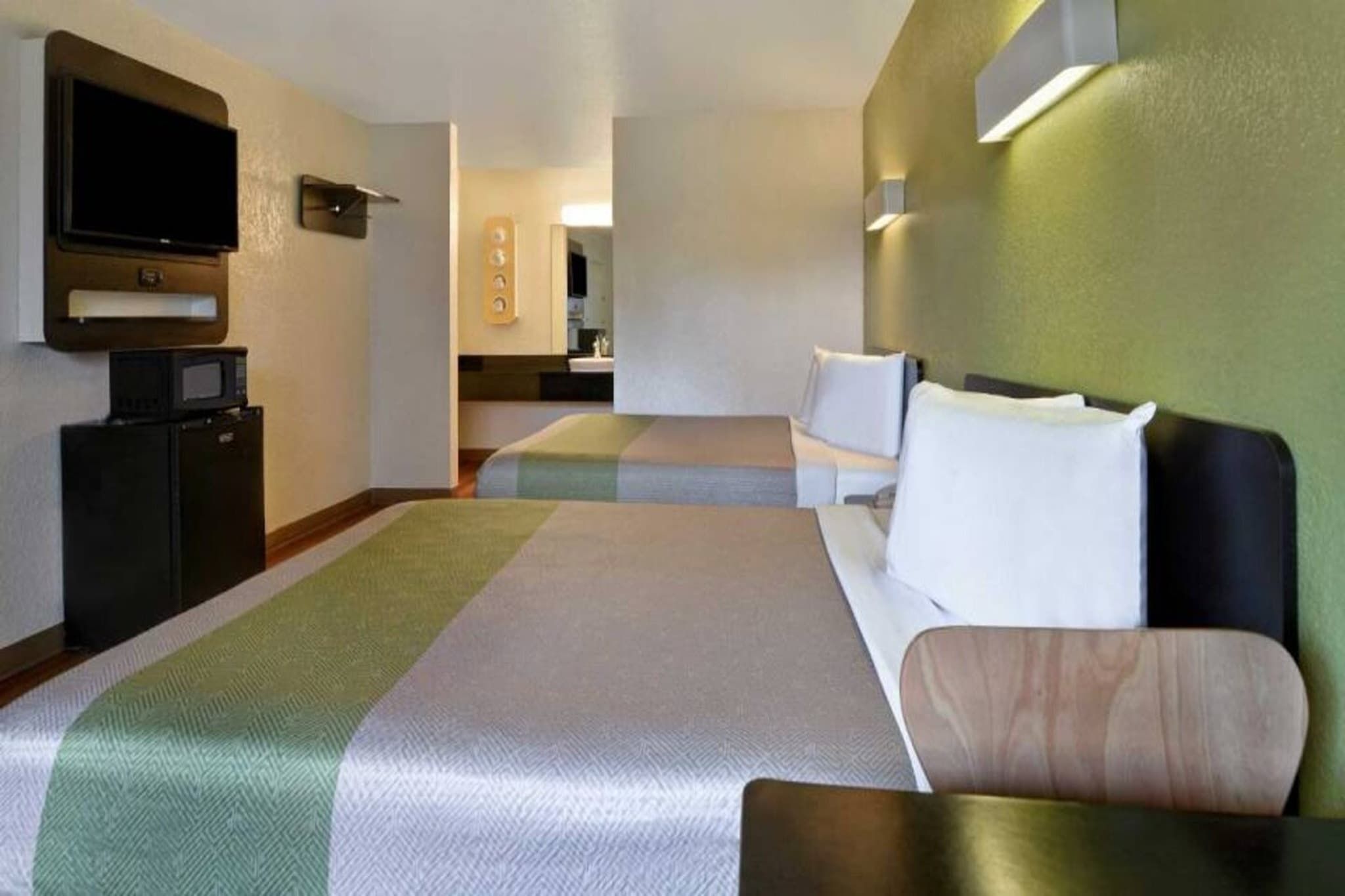 A hotel room with two beds, a television, a microwave, and a small kitchenette.