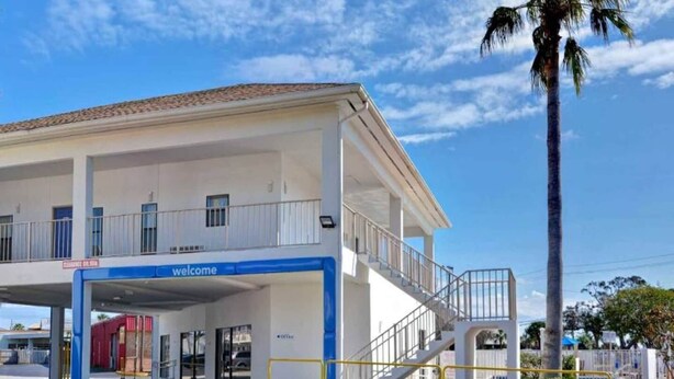 Un edificio con un cartel de 'welcome', un vestíbulo cubierto y una escalera que conduce a un nivel superior.