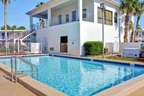 A swimming pool adjacent to a white building with balconies, palm trees, and a clear sky. - Clean 2-bed Queen|Free Wifi&Parking (Destin)