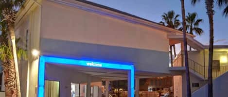 A hotel entrance with a 'Welcome' sign, a covered walkway, and a parking area.