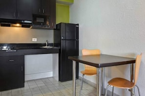 Kompakti keittiö, jossa on ruokapöytä ja -tuolit, jääkaappi ja kaapit.