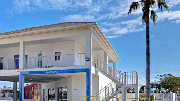 A building with a 'welcome' sign, a covered entrance, and a staircase leading to an upper level. - 2 Queen Beds | ADA/Tub/Micfridge (Destin)
