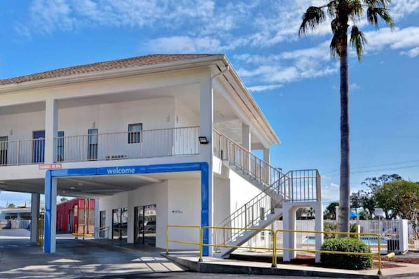 A building with a 'welcome' sign, a covered entrance, and a staircase leading to an upper level. - 2 Queen Beds | ADA/Tub/Micfridge (Destin)