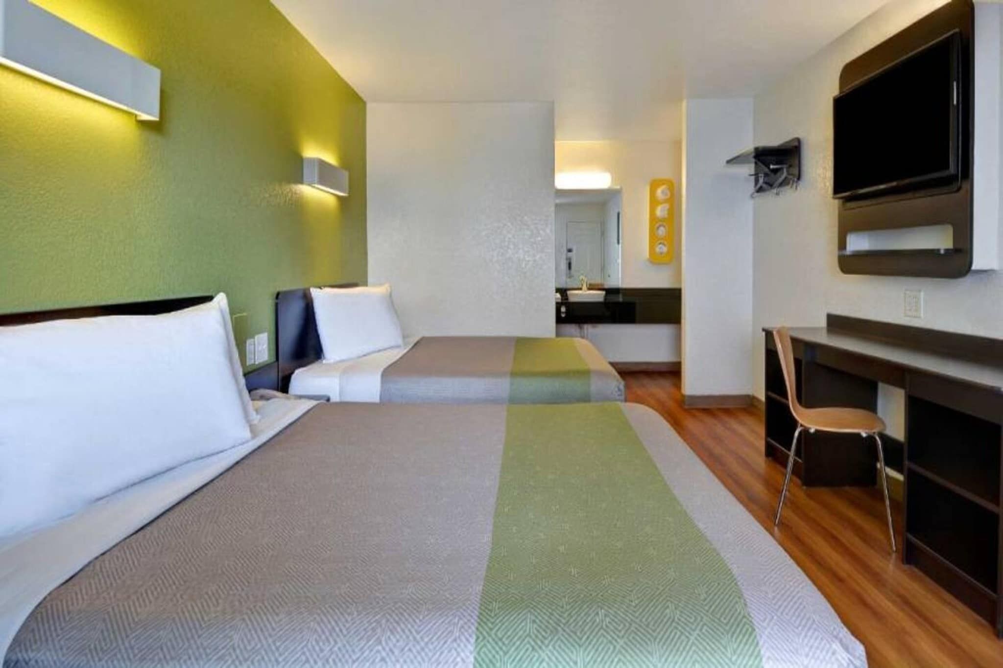 A hotel room with two beds, a desk, a chair, a television, and a kitchenette.