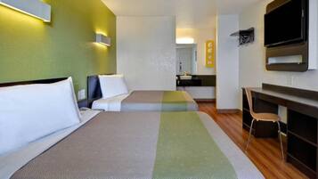 A hotel room with two beds, a desk, a chair, a television, and a kitchenette.