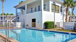 A swimming pool adjacent to a white building with balconies, a covered outdoor area, and palm trees. - 2 Queen Beds | ADA/Tub/Micfridge (Destin)