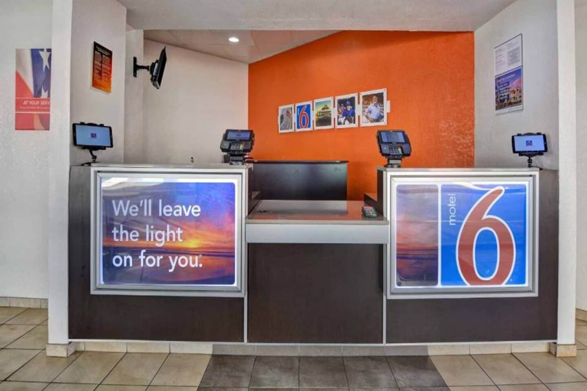 A hotel reception desk with a digital screen displaying a message, a number '6' sign, and a wall with framed pictures.