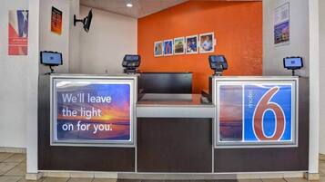 A hotel reception desk with a digital screen displaying a message, a number '6' sign, and a wall with framed pictures.