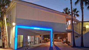 A hotel entrance with a 'Welcome' sign, a covered walkway, and a parking area. - 2 Queen Beds | ADA/Tub/Micfridge (Destin)