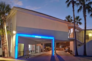 A hotel entrance with a 'Welcome' sign, a covered walkway, and a parking area. - 2 Queen Beds | ADA/Tub/Micfridge (Destin)