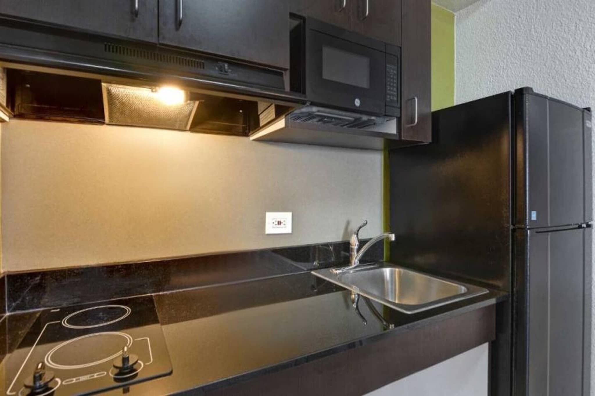 A modern kitchen with a black refrigerator, stainless steel sink, and a microwave above the counter.