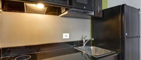 A modern kitchen with a black refrigerator, stainless steel sink, and a microwave above the counter.