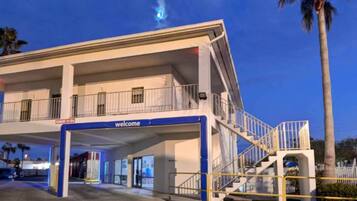 A hotel entrance with a 'welcome' sign, a covered parking area, and a staircase leading to the upper level.