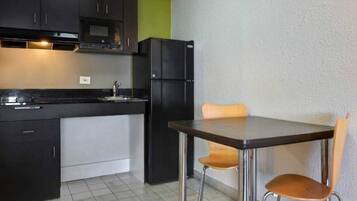A compact kitchen with a dining table and chairs, a refrigerator, and cabinets.