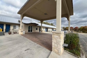 A building with a covered entrance, a parking lot, and a building with a blue door in the background. - Spacious King Bed|Coffee Machine (Junction)