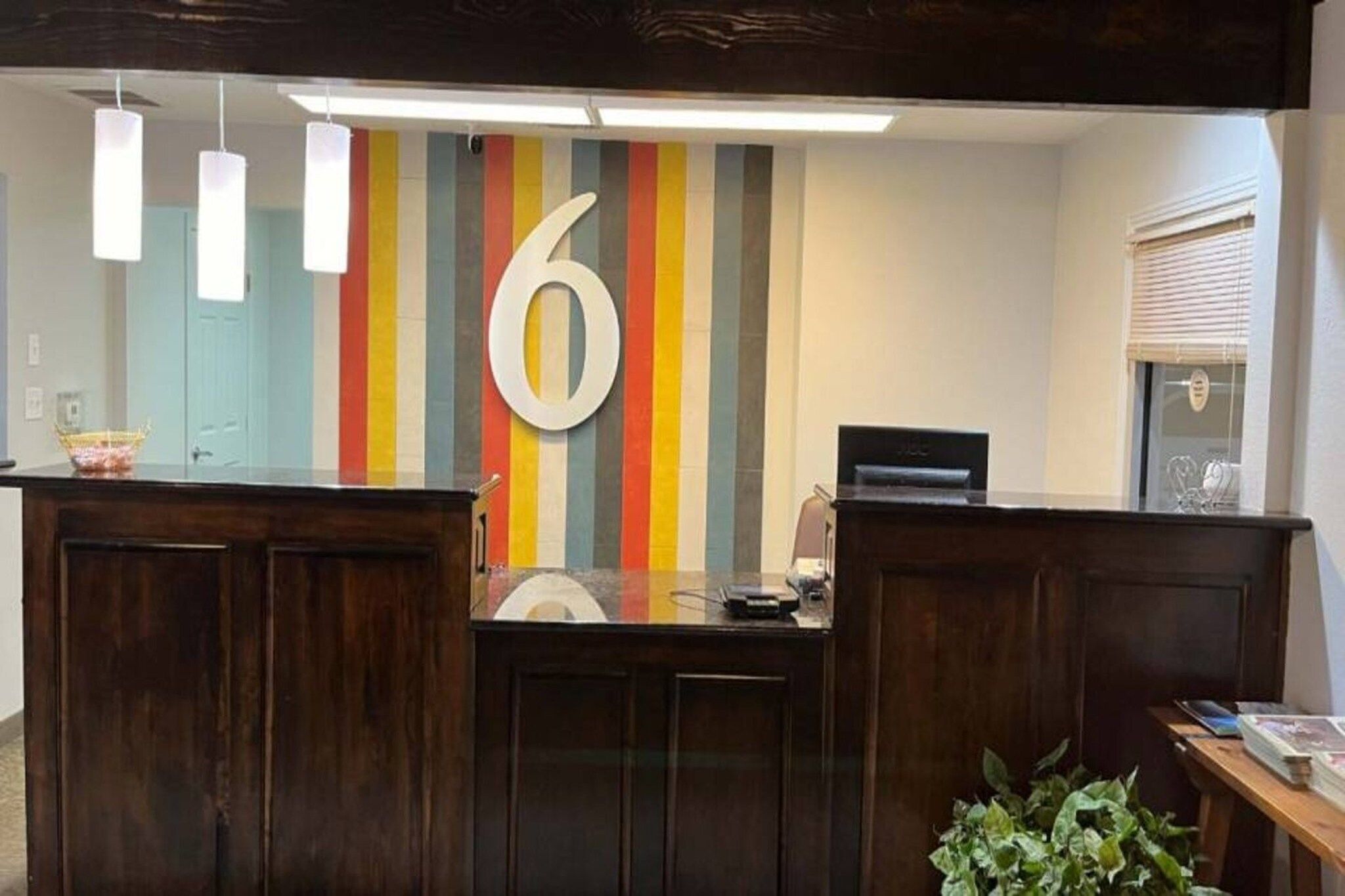Een receptiebalie met een kleurrijke gestreepte wand, een groot bord met het cijfer '6', houten lambrisering en een potplant.